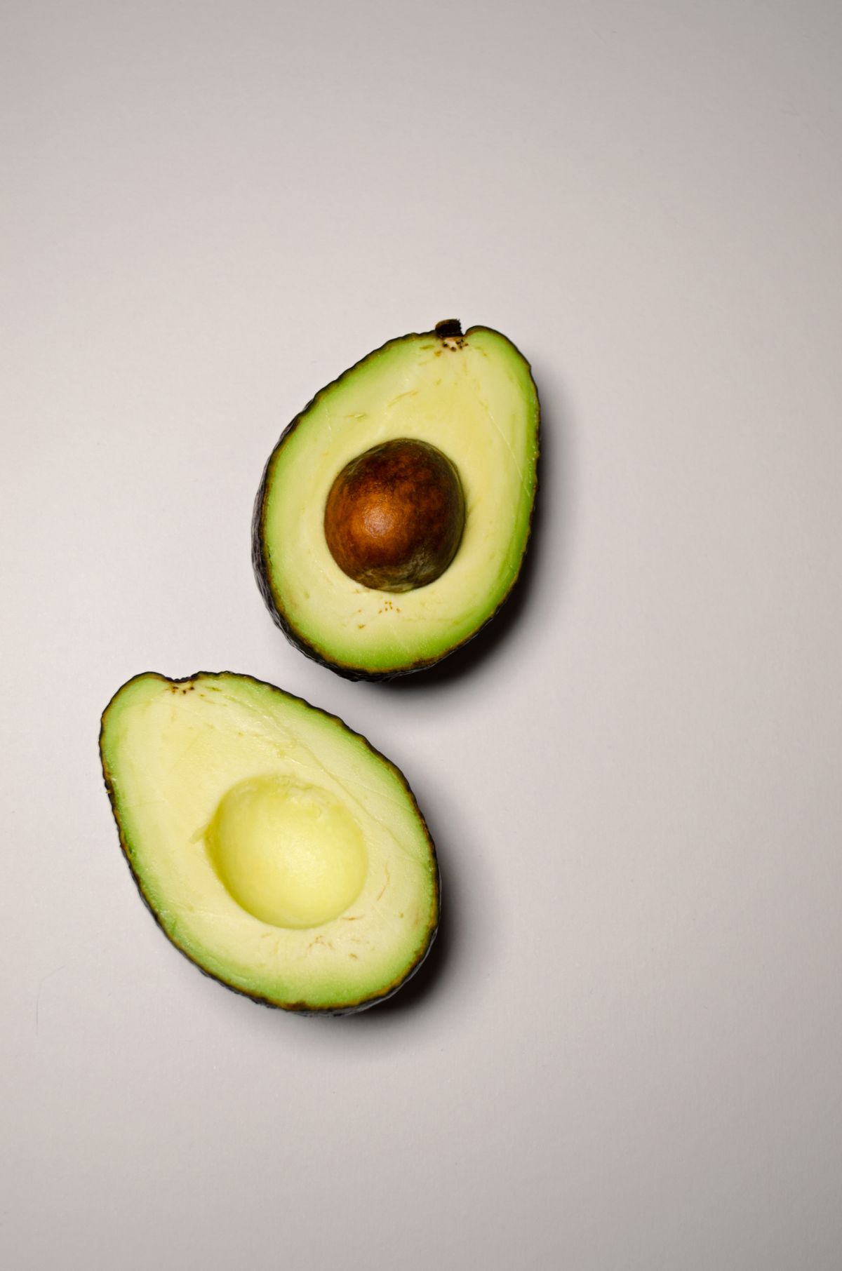 Two fresh avocado halves on a neutral background