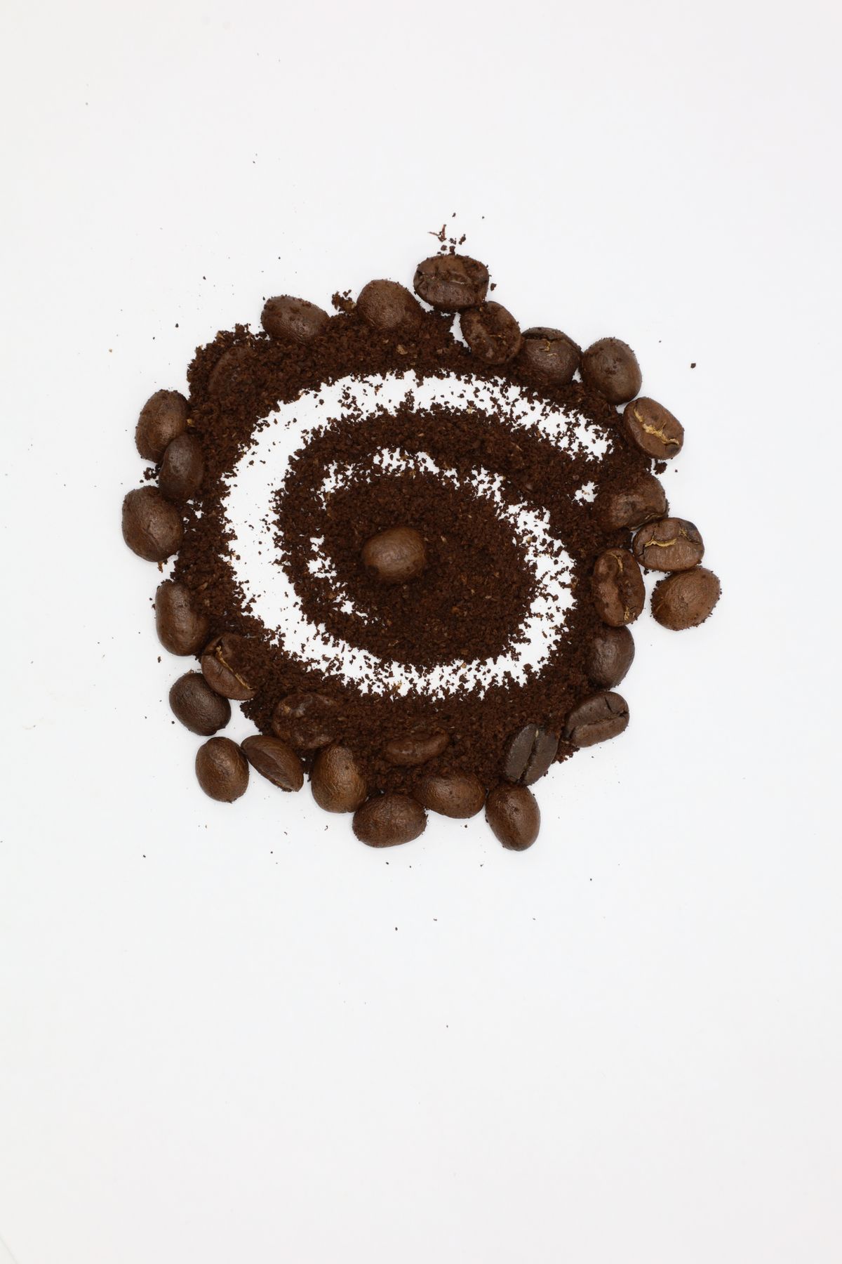 Roasted coffee beans and coffee grounds arranged on a white surface
